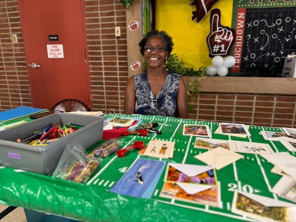 A district staff member sitting at a table with coloring pencils, pencils and cards at Goode PreK-8's Back to School Night.