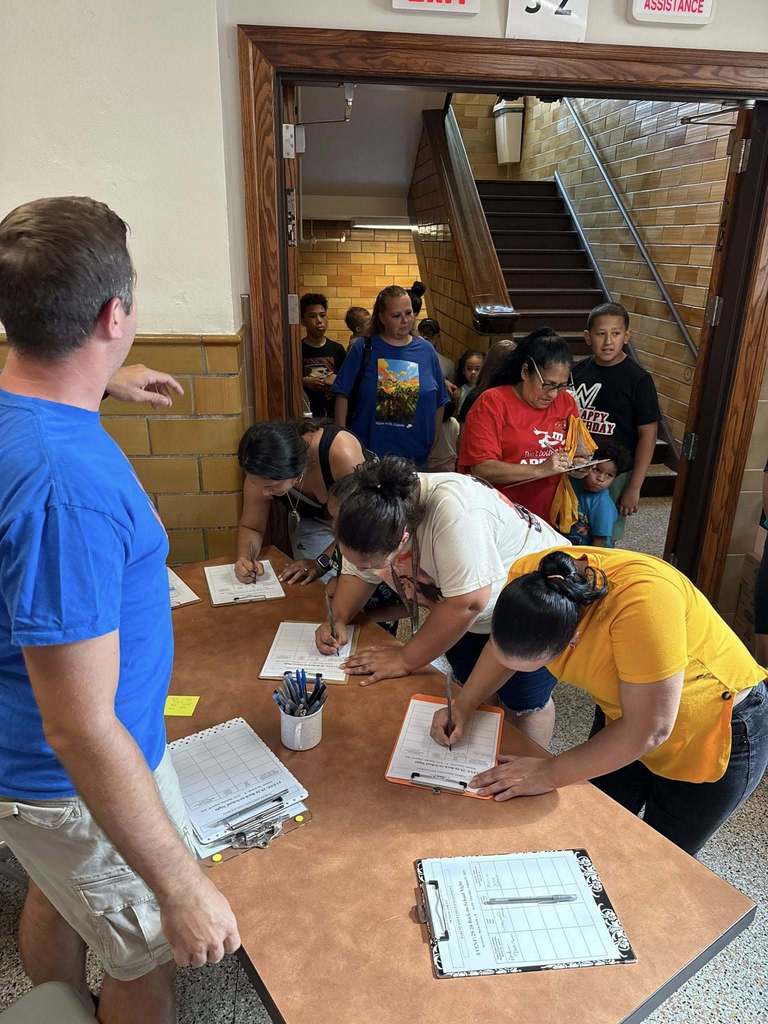 A group of people standing in a hallway while some of the people are filling out forms at a table at Davis PreK-8's Back to School Night.