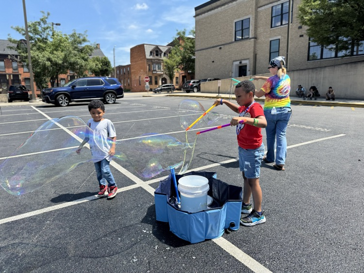 Two children and one adult blowing bubbles in a parking lot.