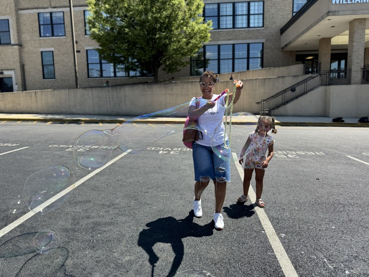 District leadership blowing a bubble with a child looking behind her in a parking lot.