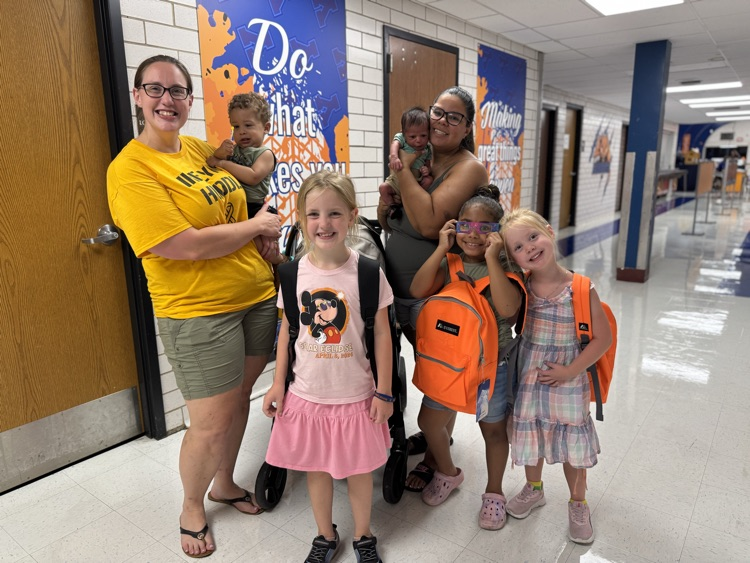 Two adults and five children posing for a photo in a school cafeteria.