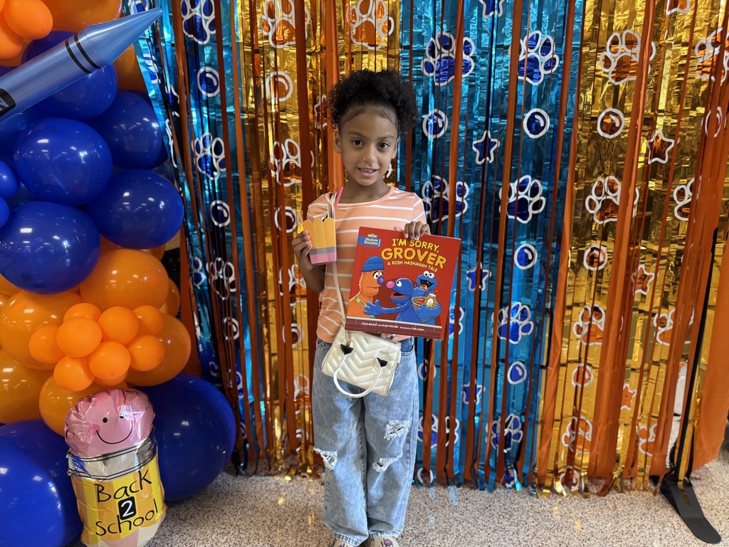 A student posing in front of a backdrop while holding up a book and a cardboard pencil container.