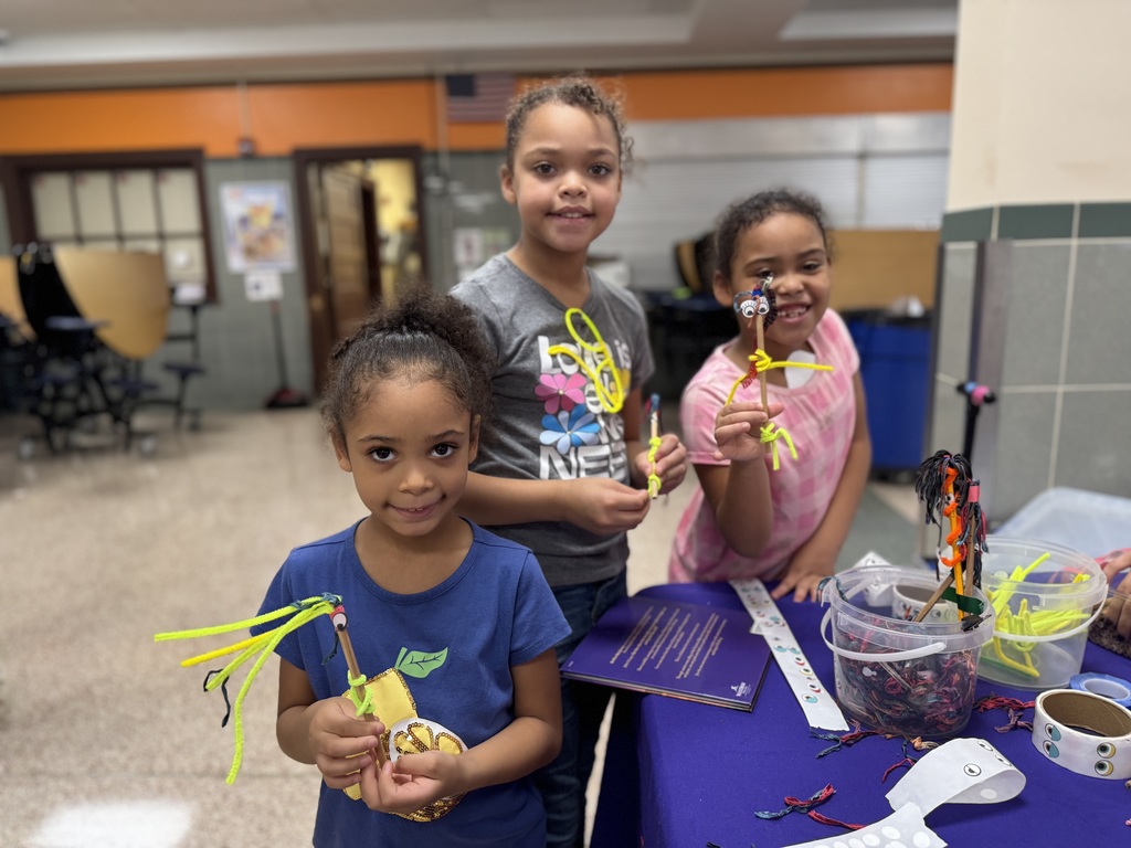 Three students posing for a photo and holding up an arts craft. 