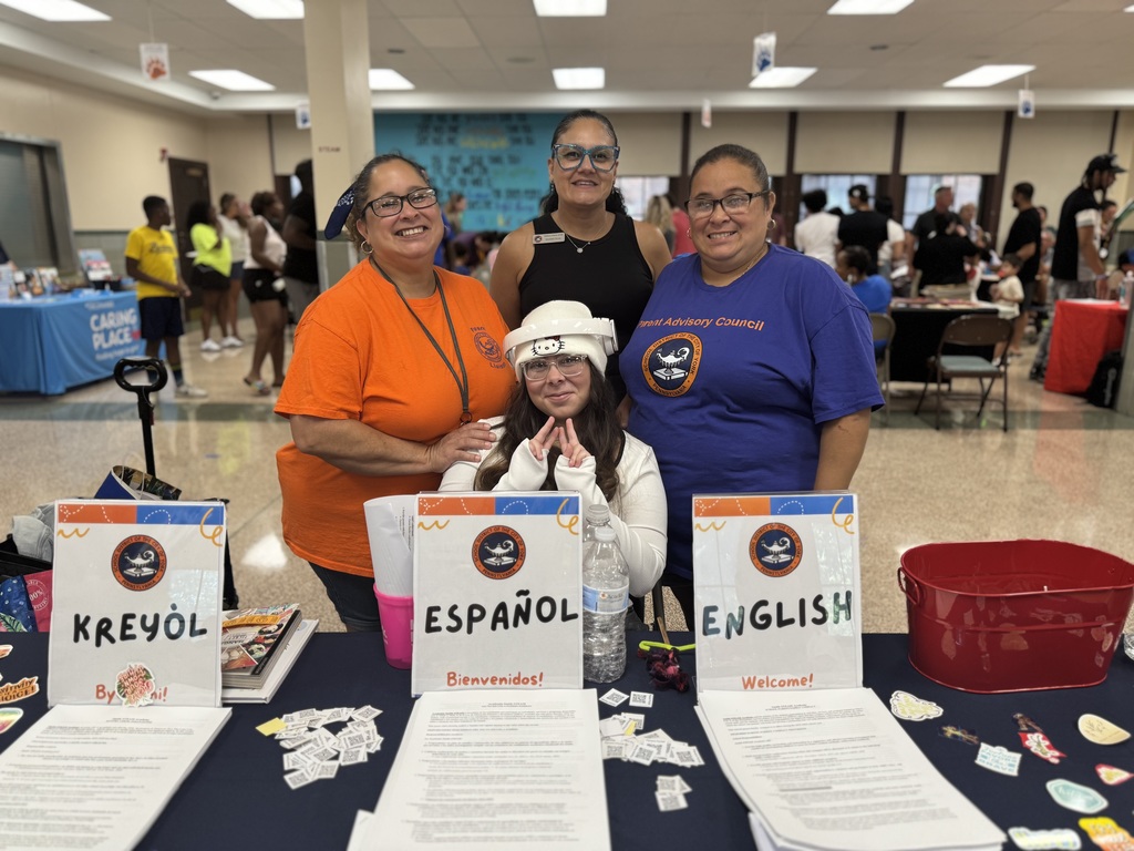 Four district staff members posing for a photo behind a table with papers on it for English, Spanish, and Haitian Creole.