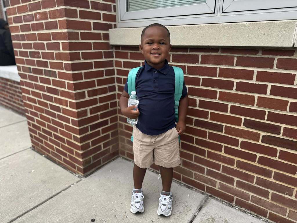 A student standing with a water bottle in his hand and a bookbag on his shoulders.