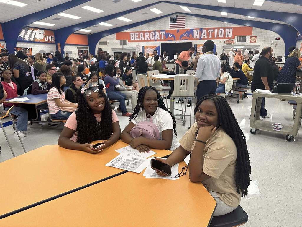 Three students sitting at a table surrounded by other people in William Penn Senior High School's cafeteria.