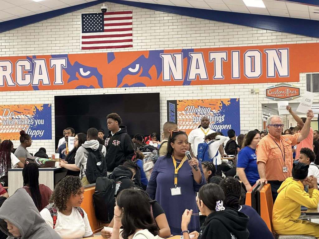 Superintendent of Schools, Dr. Andrea Berry-Brown holding a microphone and speaking in William Penn Senior High School's cafeteria.