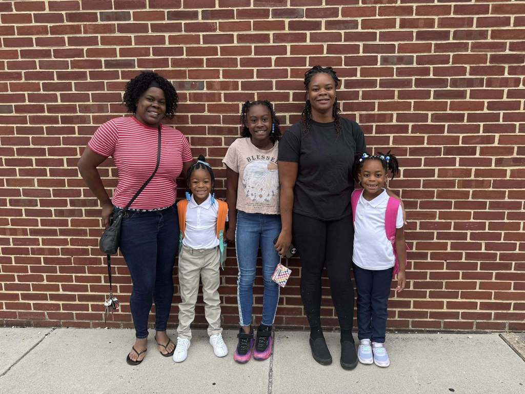 Two adults and three children posing in front of a brick wall outside.