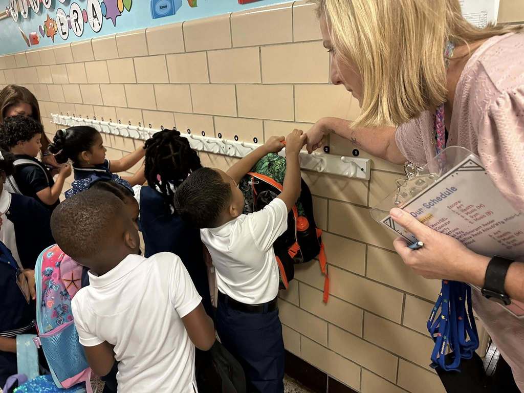 A district staff member at Devers PreK-8 helping students hang up their bookbags on hooks.