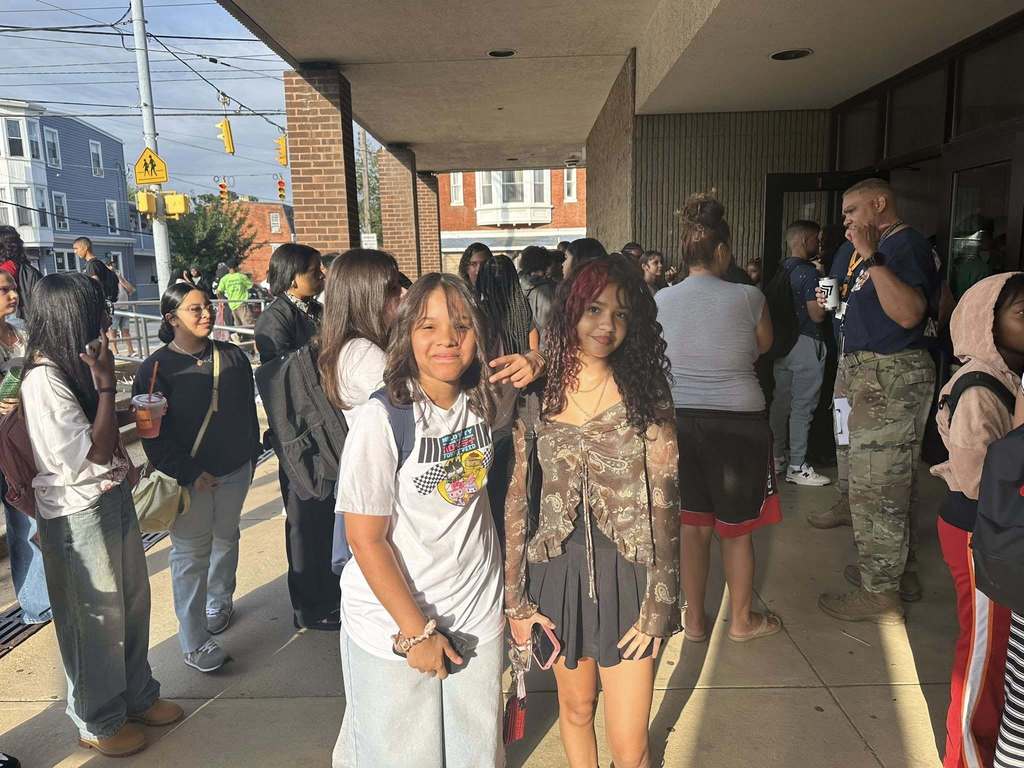 Two students posing together outside surrounded by a crowd of people.