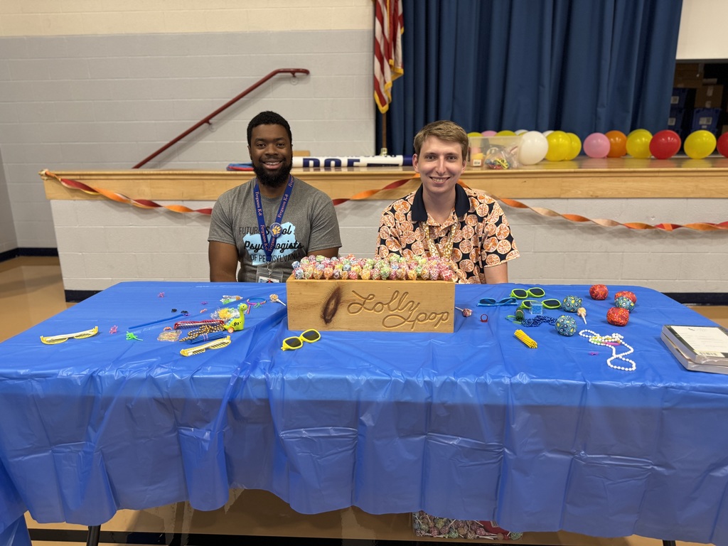 Two district staff members sitting at a table with candy and toys during Ferguson PreK-8's Back to School Night.