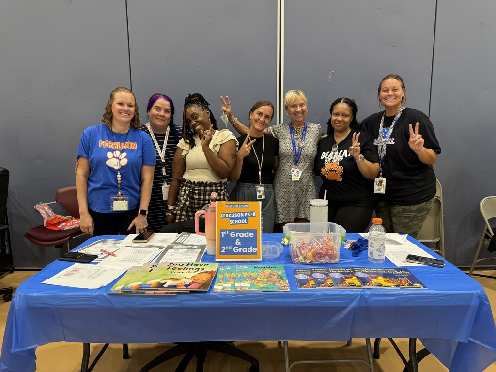 Seven district staff members posing for a photo during Ferguson PreK-8's Back to School Night. Some of the staff members are holding up peace signs.