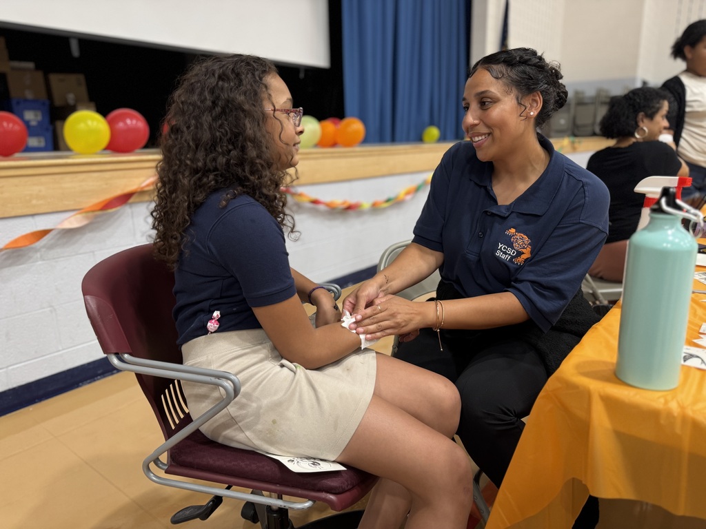 A district staff member putting a waterproof sticker on a student at Ferguson PreK-8's Back to School Night.