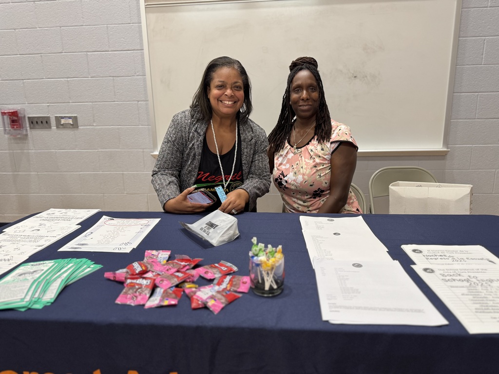 Superintendent of Schools, Dr. Andrea Berry-Brown posing next to a district staff member behind a table with papers and candy on it during Ferguson PreK-8's Back to School Night.