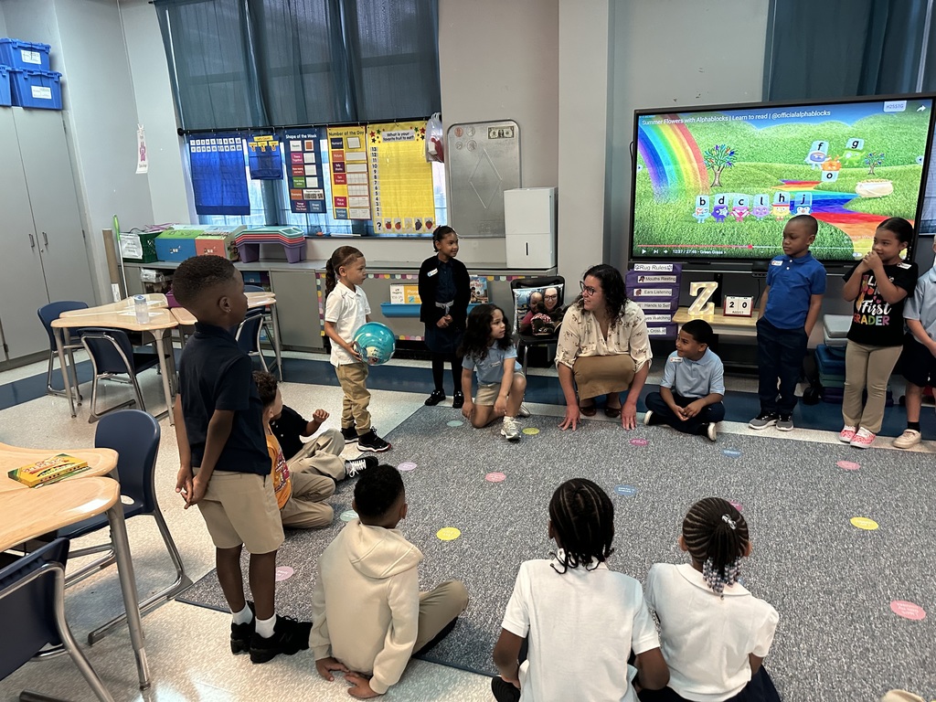 A teacher and a classroom of students. One of the students is holding a ball in his hand.