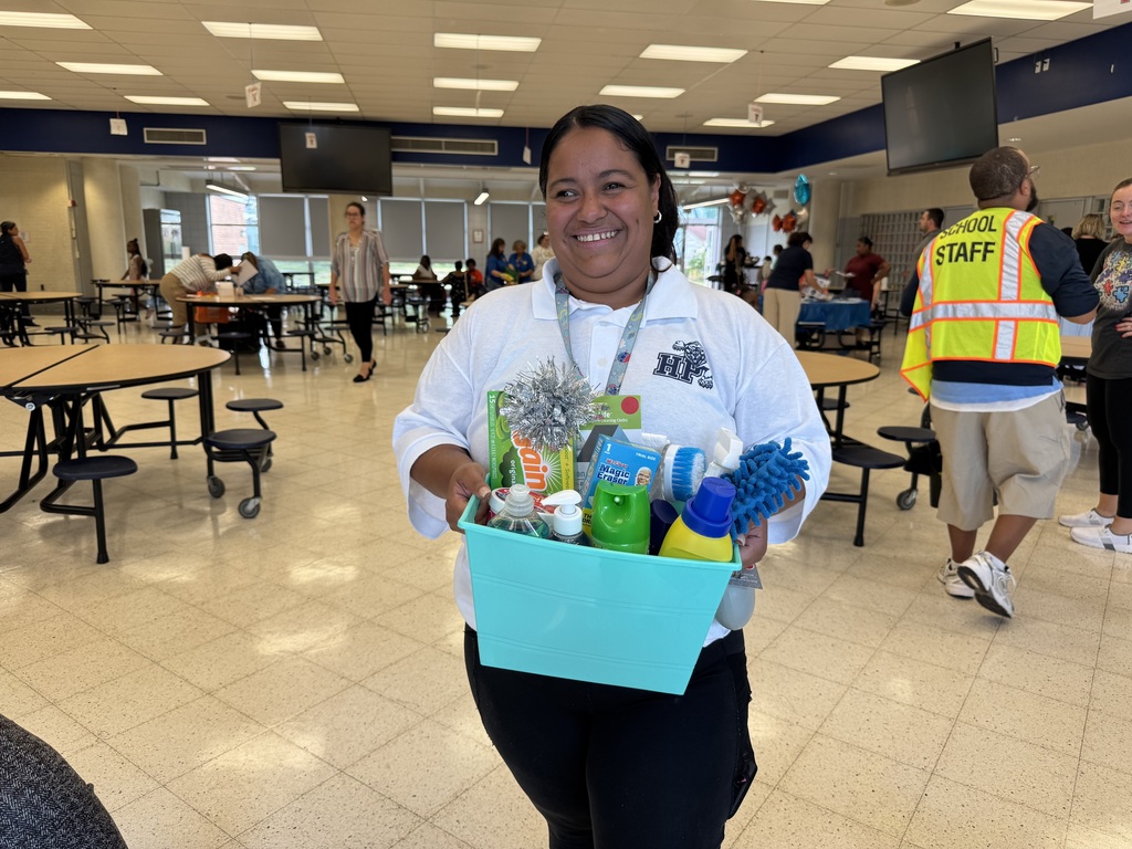 A district staff member holding up a basket containing cleaning supplies at Hannah Penn's recent Back to School Night. People can be seen in the background.
