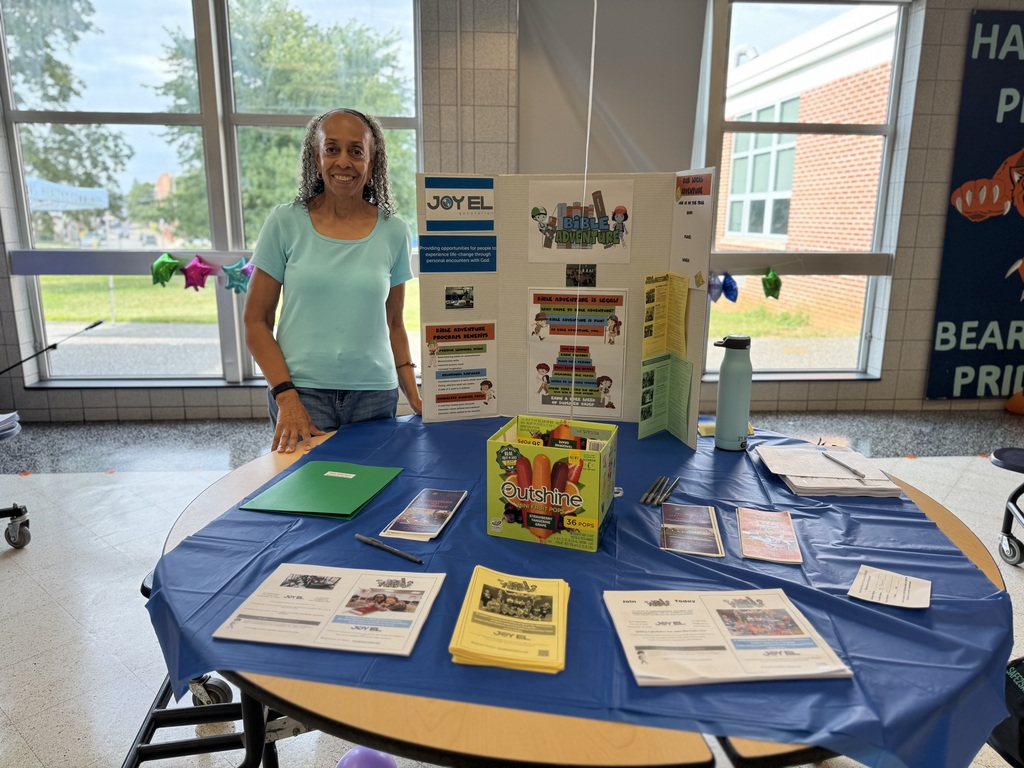 A community member with the Joy El Program posing next to a table with resources for the Joy El Program at Hannah Penn's recent Back to School Night.