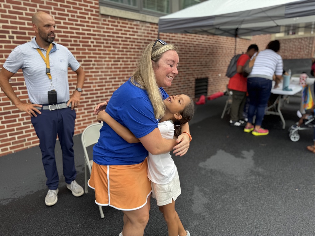 A district staff member and a student hugging each other. People can be seen in the background.