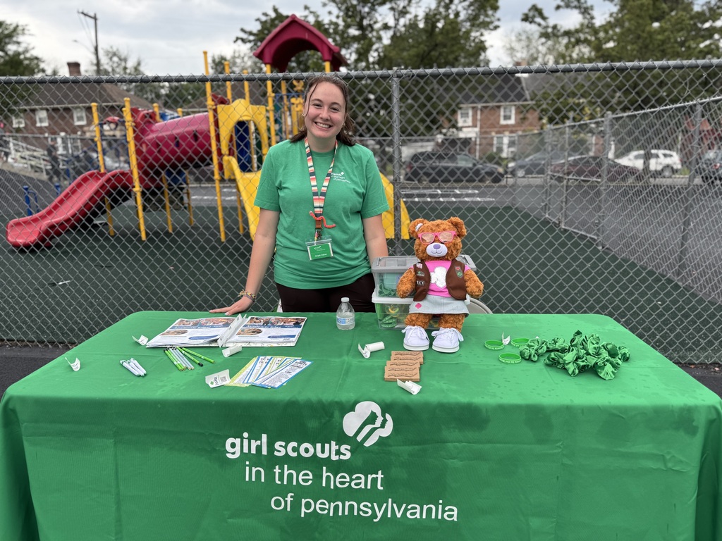 A girl scout employee posing at a table that has different materials on it.