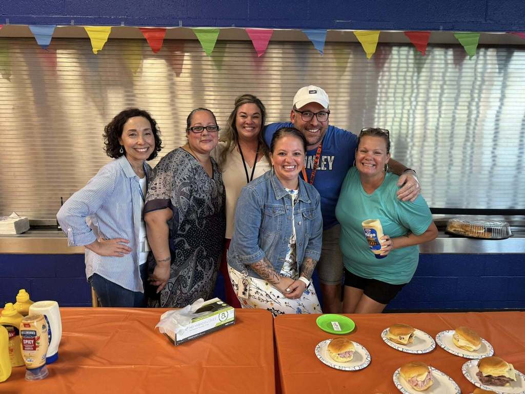 McKinley PreK-8 Principal, Dr. Ashley White and district staff members posing behind a table that has sandwiches and condiments on it.