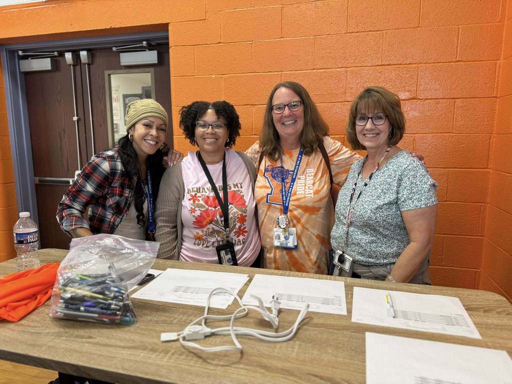 District staff members posing in front of an orange well while standing behind a table with papers, pens and a cord on it.