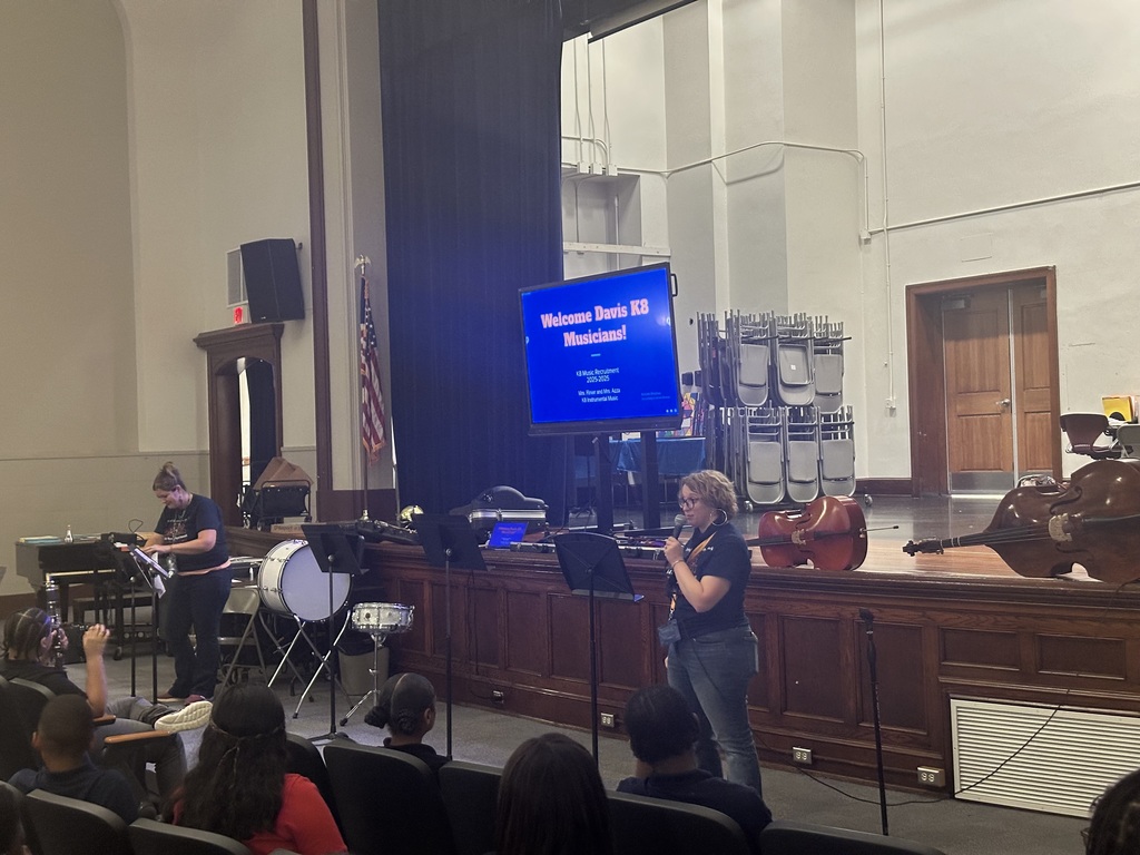 District staff member speaking into a microphone during the district's annual K-8 Music Recruitment Assembly.