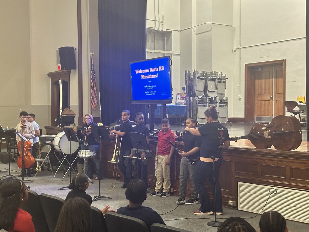 A student speaking into a microphone while standing in a line with other students during the district's annual K-8 Music Recruitment Assembly.