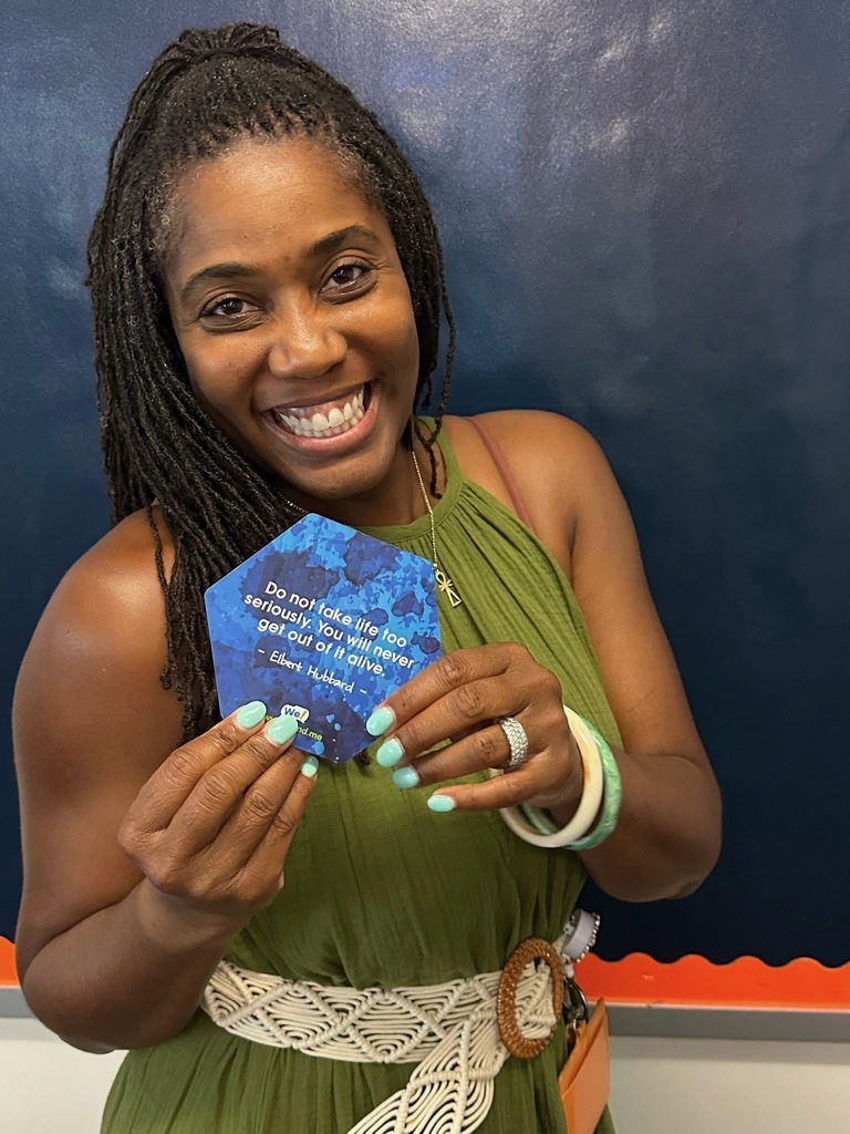 A district staff member holding up an inspirational quote while standing in front of a bulletin board.