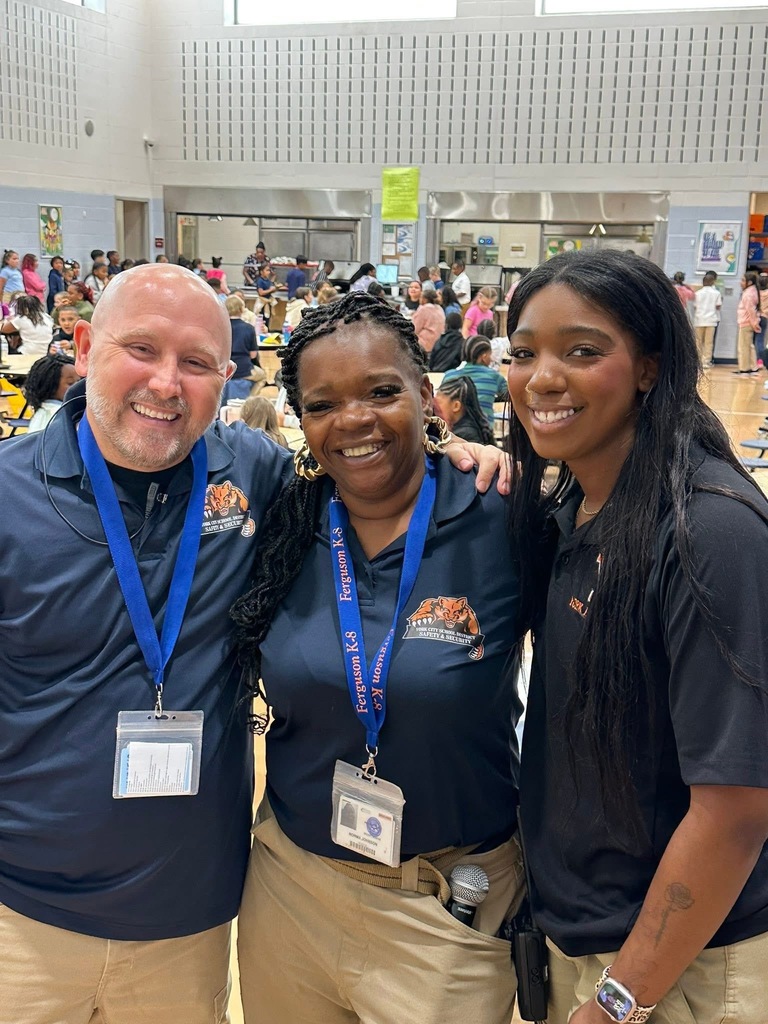 District staff members posing together for a photo. Students can be seen in the background.