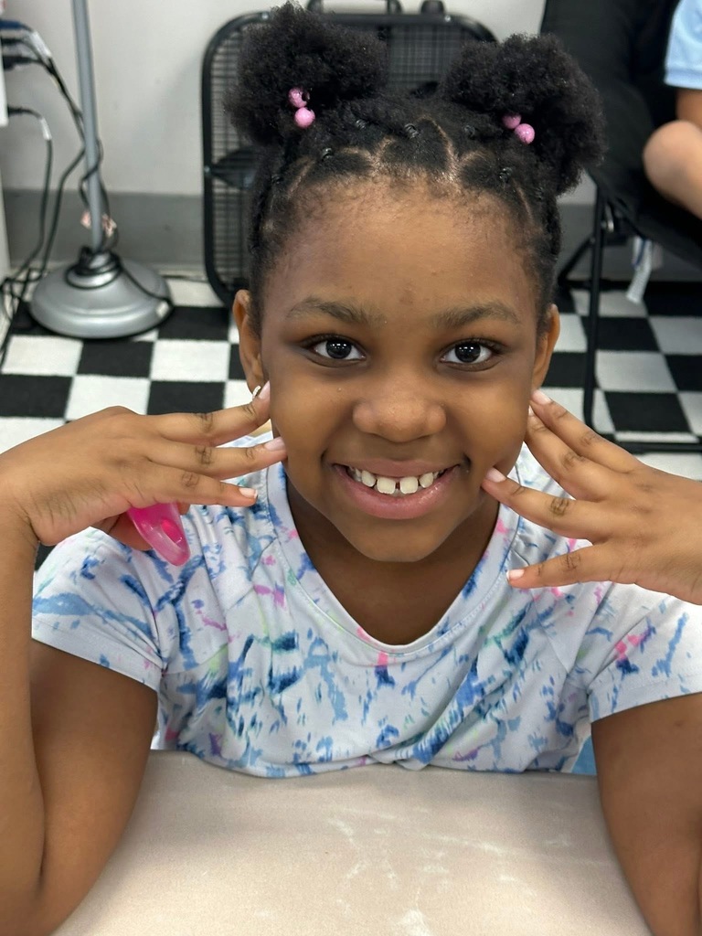 A student smiling with both of her hands on her face. 