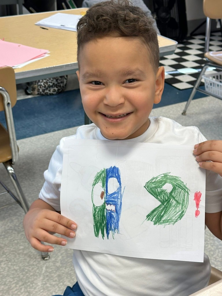 A student smiling and holding up a drawing. 