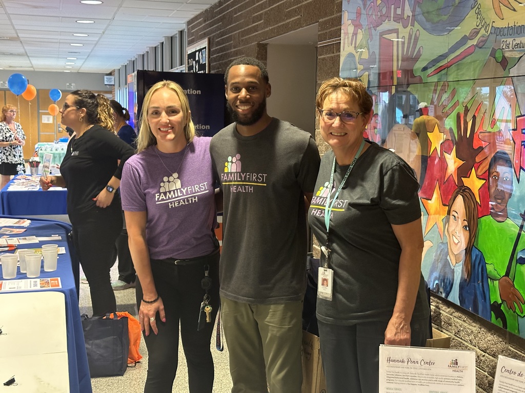 Three district staff members posing for a group photo. Other people can be seen in the background.