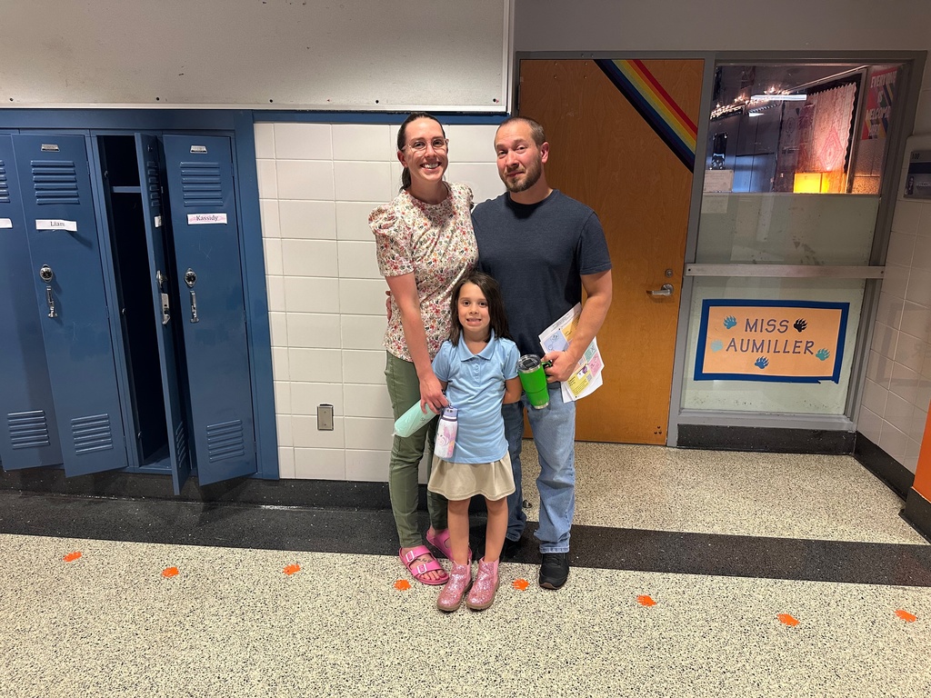 Two adults and one child standing near a classroom and dark blue lockers. 