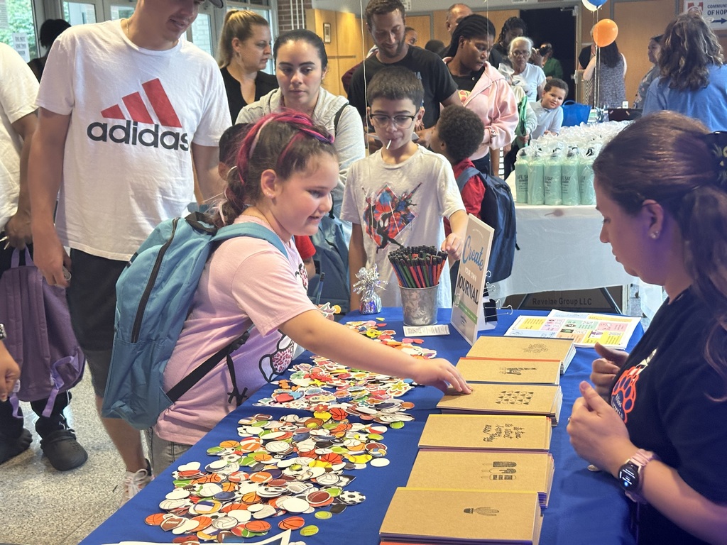 A child reaching for a journal. Multiple people can be seen in the background.