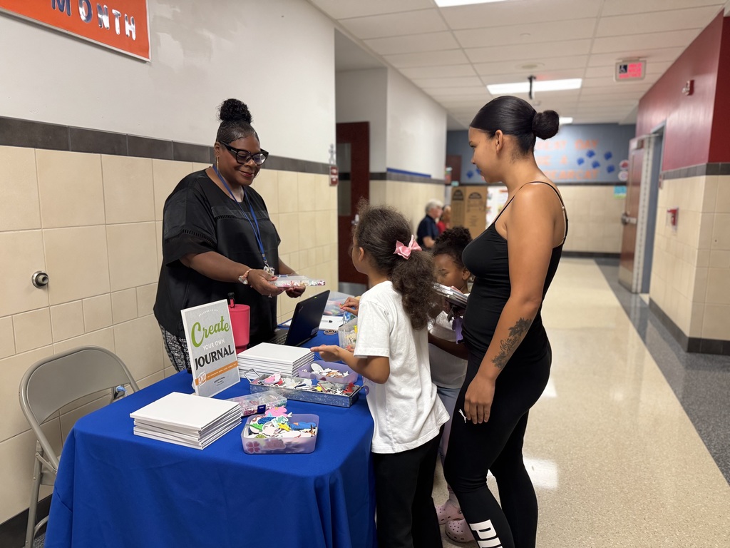 A district staff member handing a container of stickers to a child. There is an adult and another child standing next to the child who is reaching for the stickers.