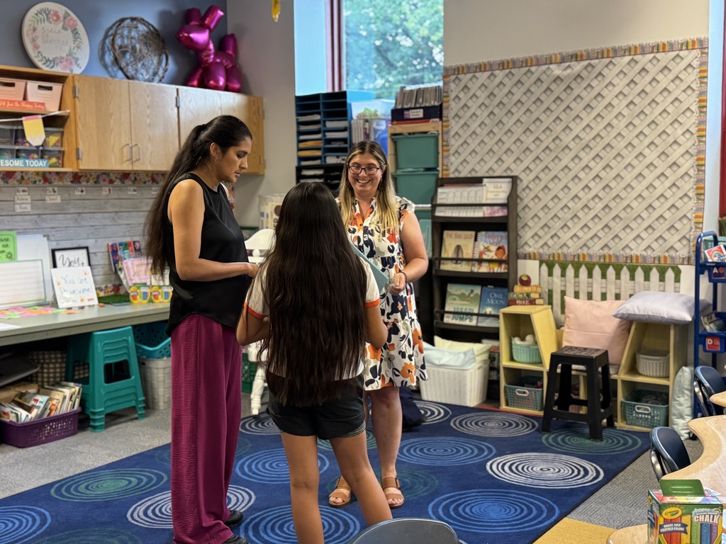 A district staff member, an adult and a child standing in a classroom. 