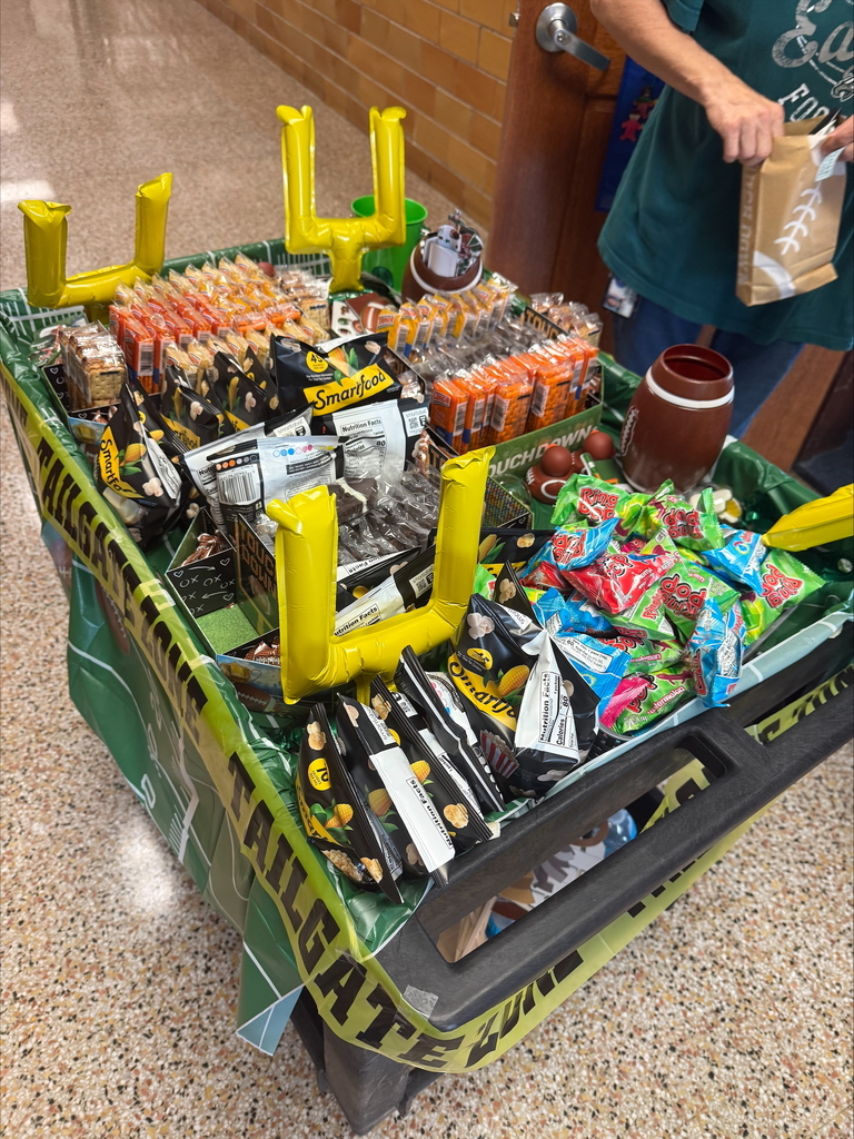 A snack cart decorated for tailgating, featuring bags of popcorn, candy, and beverages, topped with festive inflatable goalposts.