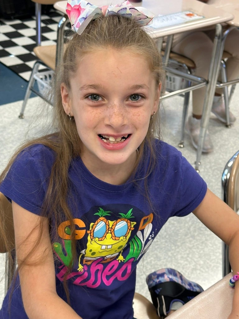 A student smiling and sitting at a desk in a classroom setting.