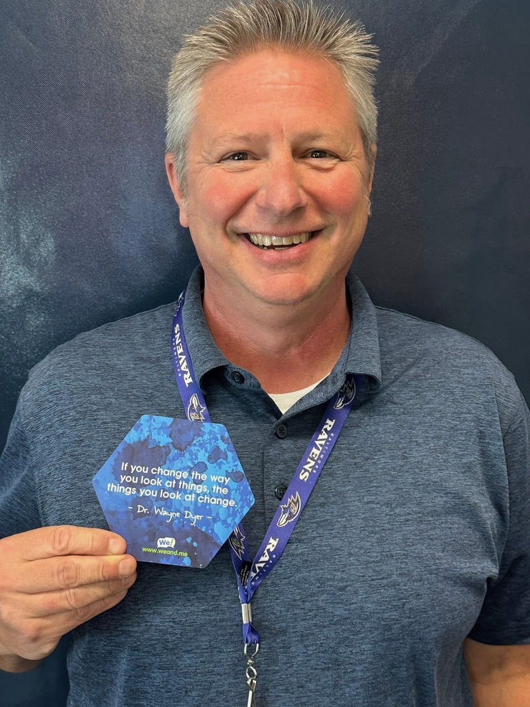 A district staff member is holding a hexagonal card with a quote by Dr. Wayne Dyer against a dark, abstract background.