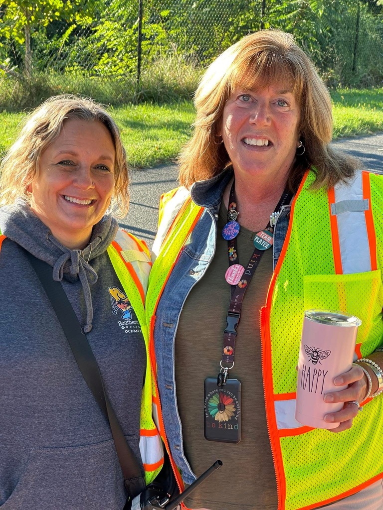 Two district staff members standing together outdoors, one holding a pink tumbler.