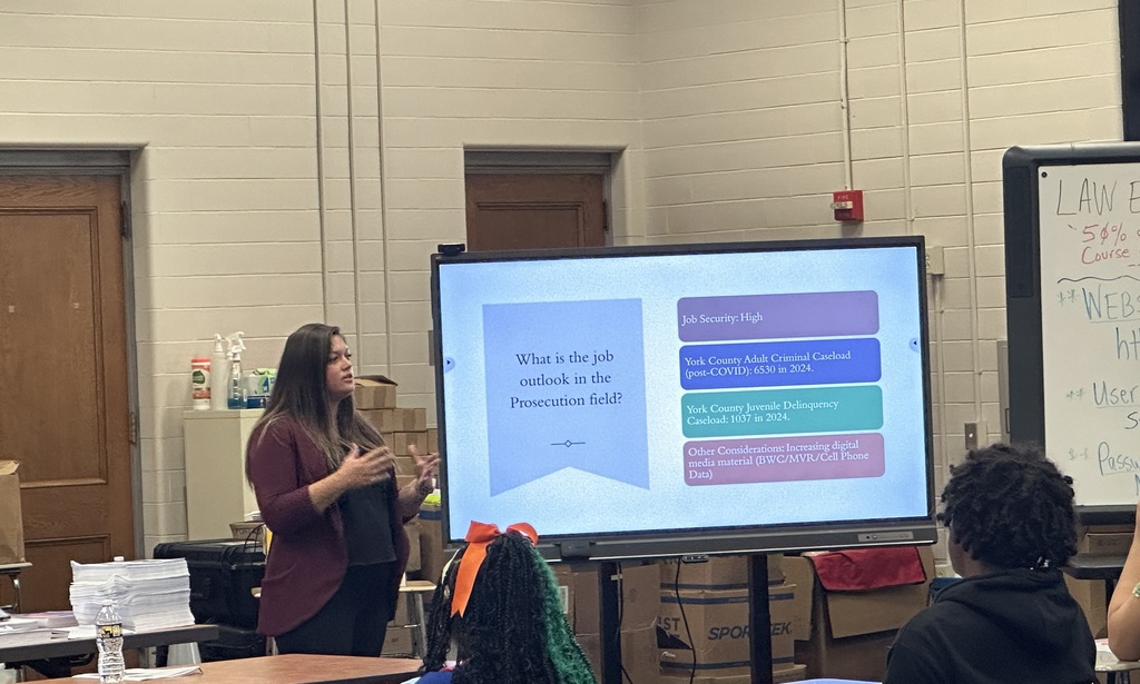 A presenter explains job outlook in the prosecution field, with a slide listing statistics and considerations in a classroom setting.
