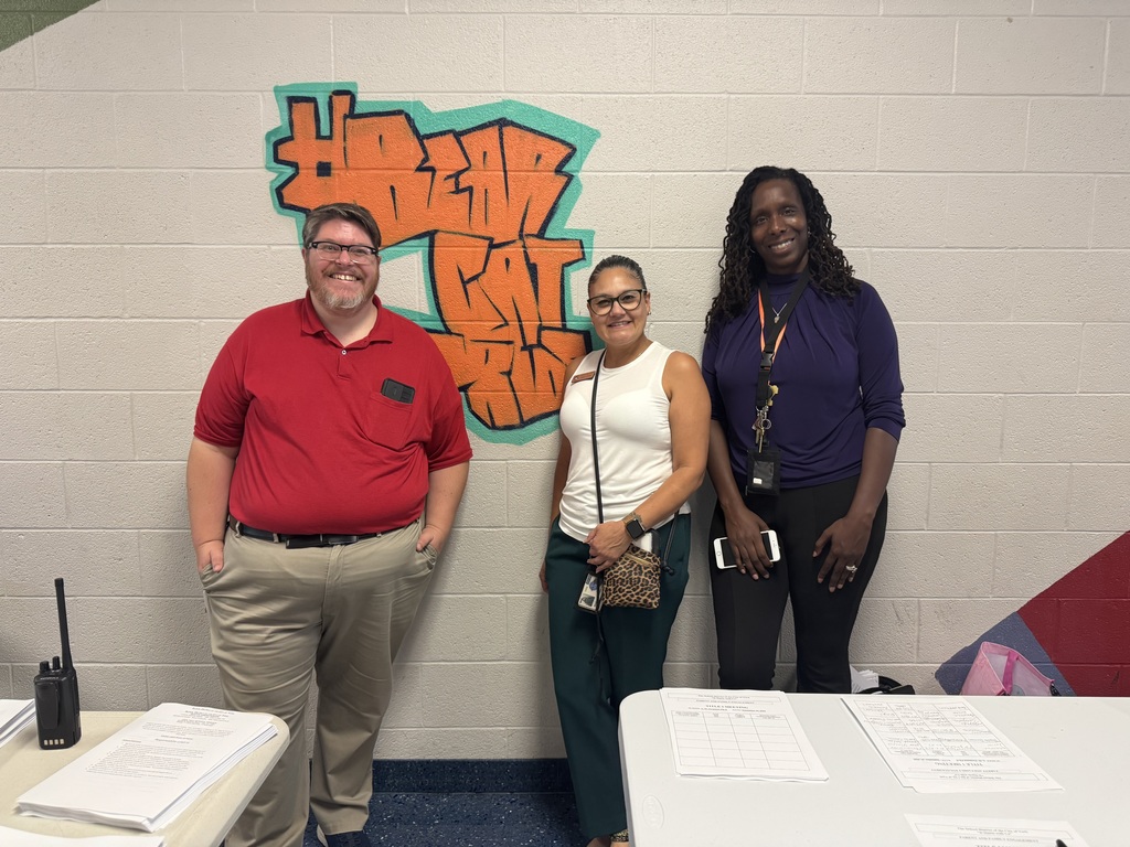 District parent liaisons and a district staff member are posing together in front of a wall that says "Bearcat Pride". Papers and a radio are on a nearby table. 