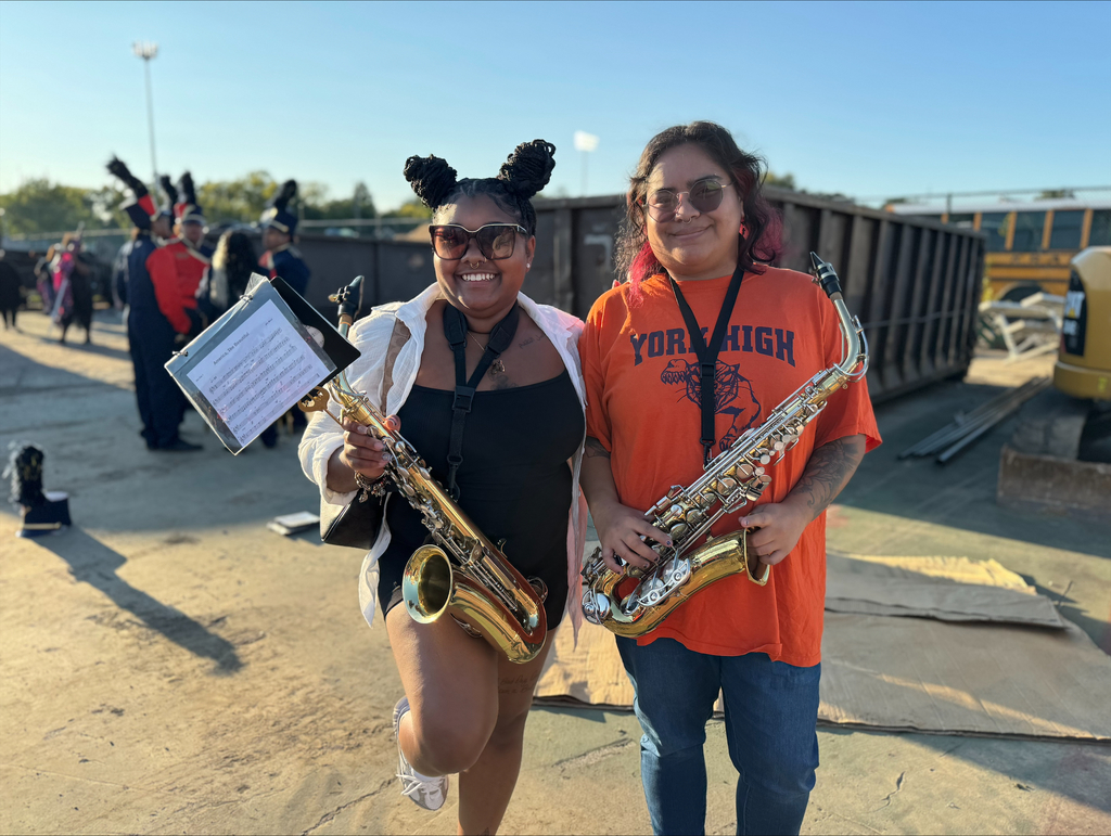 Two York High band members posing together while holding instruments in an outdoor setting, with people in the background.