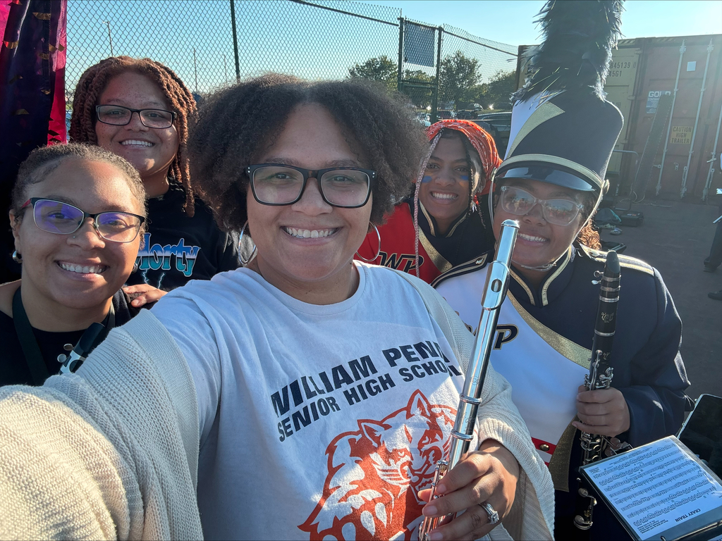 Two district staff members and York High band members posing together in an outdoor setting. One of the district staff members is holding an instrument.