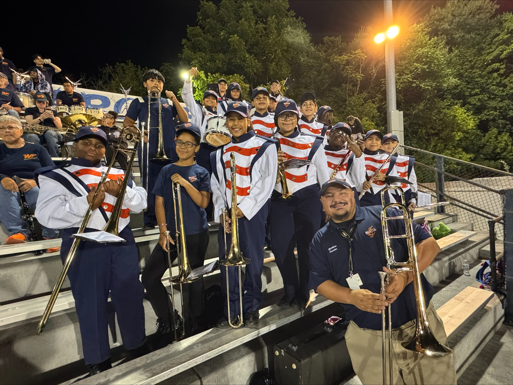 York High band posing on stadium bleachers, dressed in matching uniforms, holding various brass instruments under stadium lights.