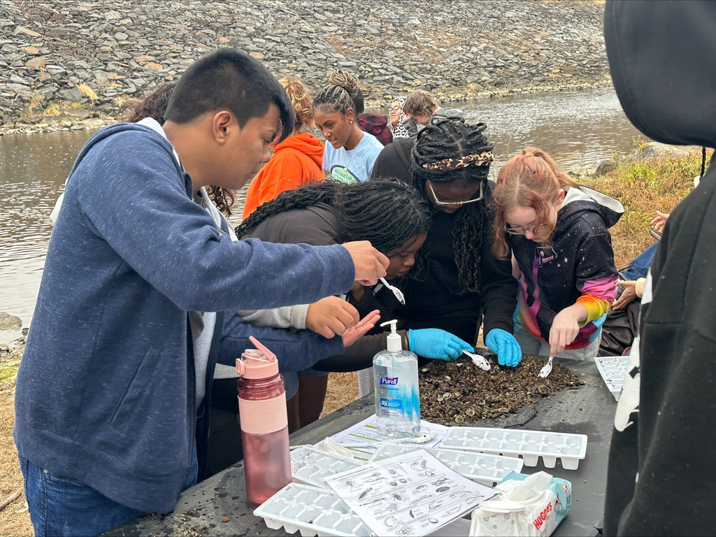 A group of students gathering around a table outside, examining materials for a science project.