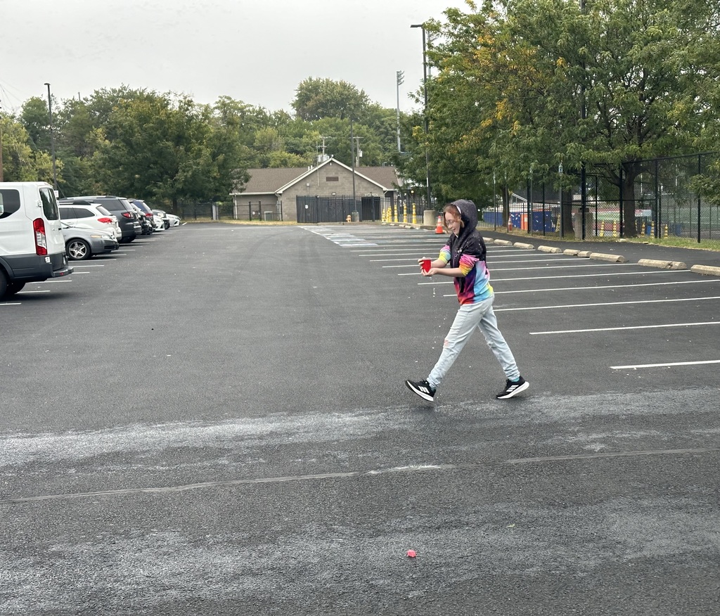 A student is walking outside while holding a cup of water in her hand.