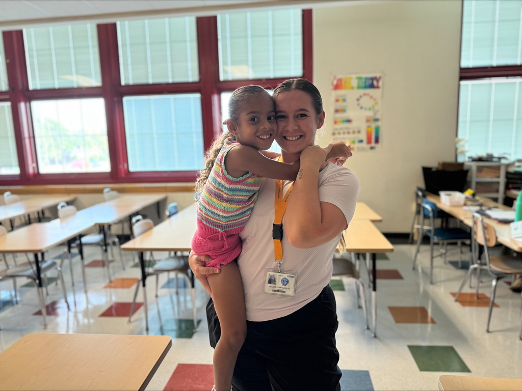 A district staff member is holding a young student in a classroom setting.