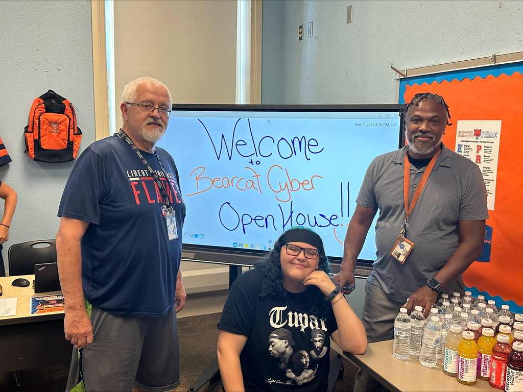 Two district staff members and a student standing in front a screen displaying the words "Welcome to Bearcat Cyber Open House" on it. They are standing near a table that has water bottles and Vitamin Water bottles on it.