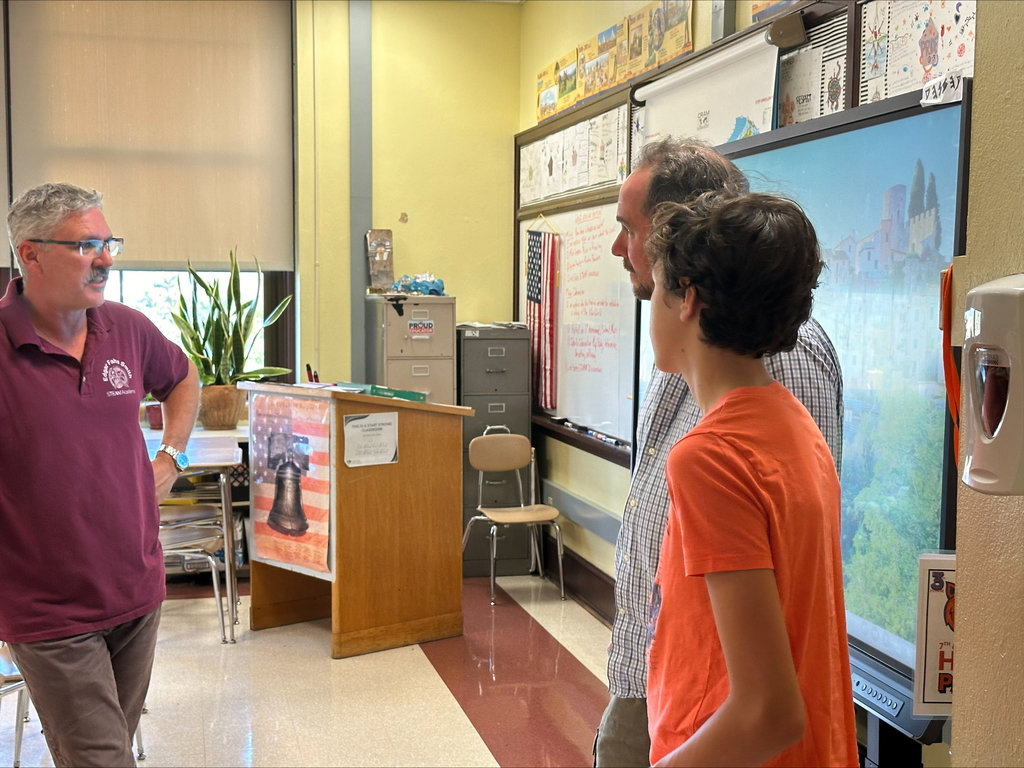 A district staff member, an adult, and a student are engaging in conversation in a classroom setting.